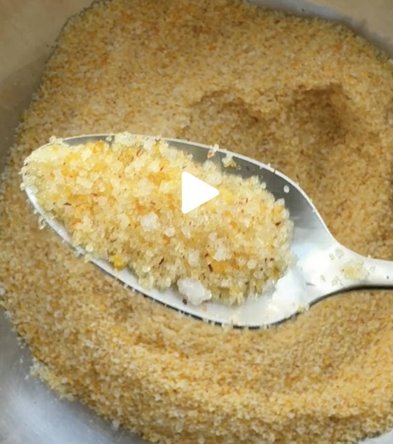 A silver spoon with golden colored salt mixture sits above a large bowl full of the same salt mixture.