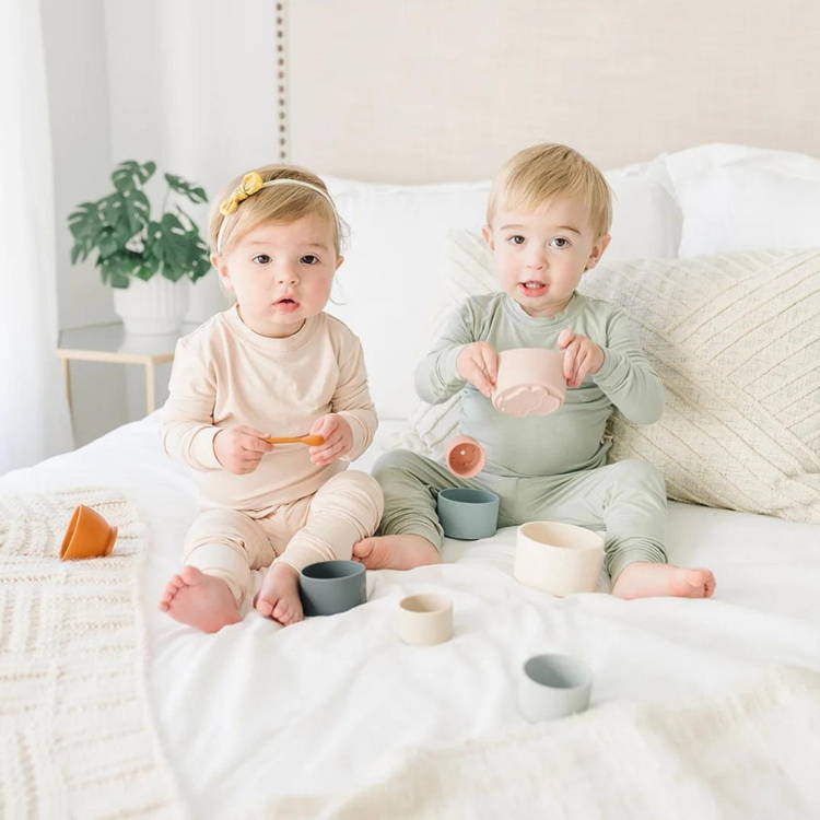 Cute baby brother and sister sitting on bed and playing with silicone stacking cups.