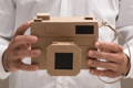 Close up on man's hands holding a camera made out of cardboard.
