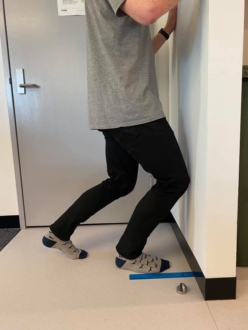 Preparing for a lunge to measure knee to wall for ankle dorsiflexion and tight calves