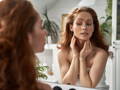 woman looking at her sensitive skin in the mirror