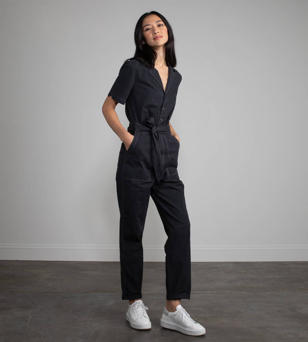 A woman wearing a clack short sleeve jumpsuit and white sneakers.