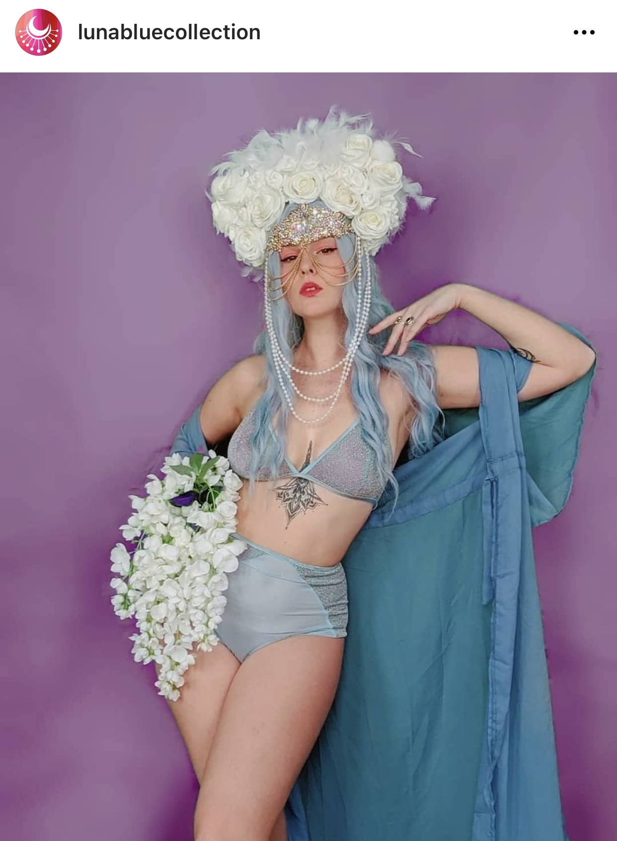 Image shows a woman in a blue festival two piece holding white flowers and wearing a white LED headdress.
