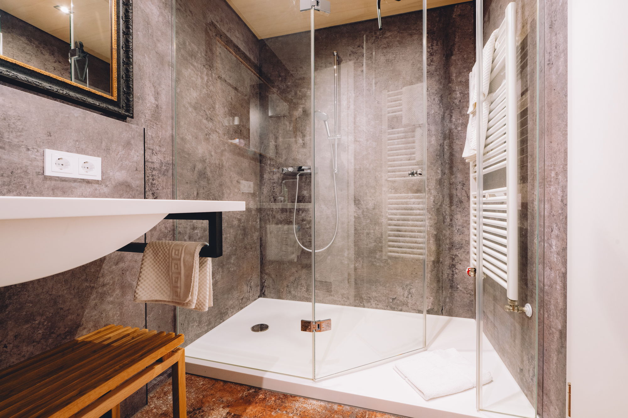 Ein modernes Badezimmer mit Steinwänden, einem schlanken Waschbecken und einer großen Dusche mit Glaswänden.