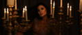 Woman with perfect facial features sitting among a room filled with burning candles