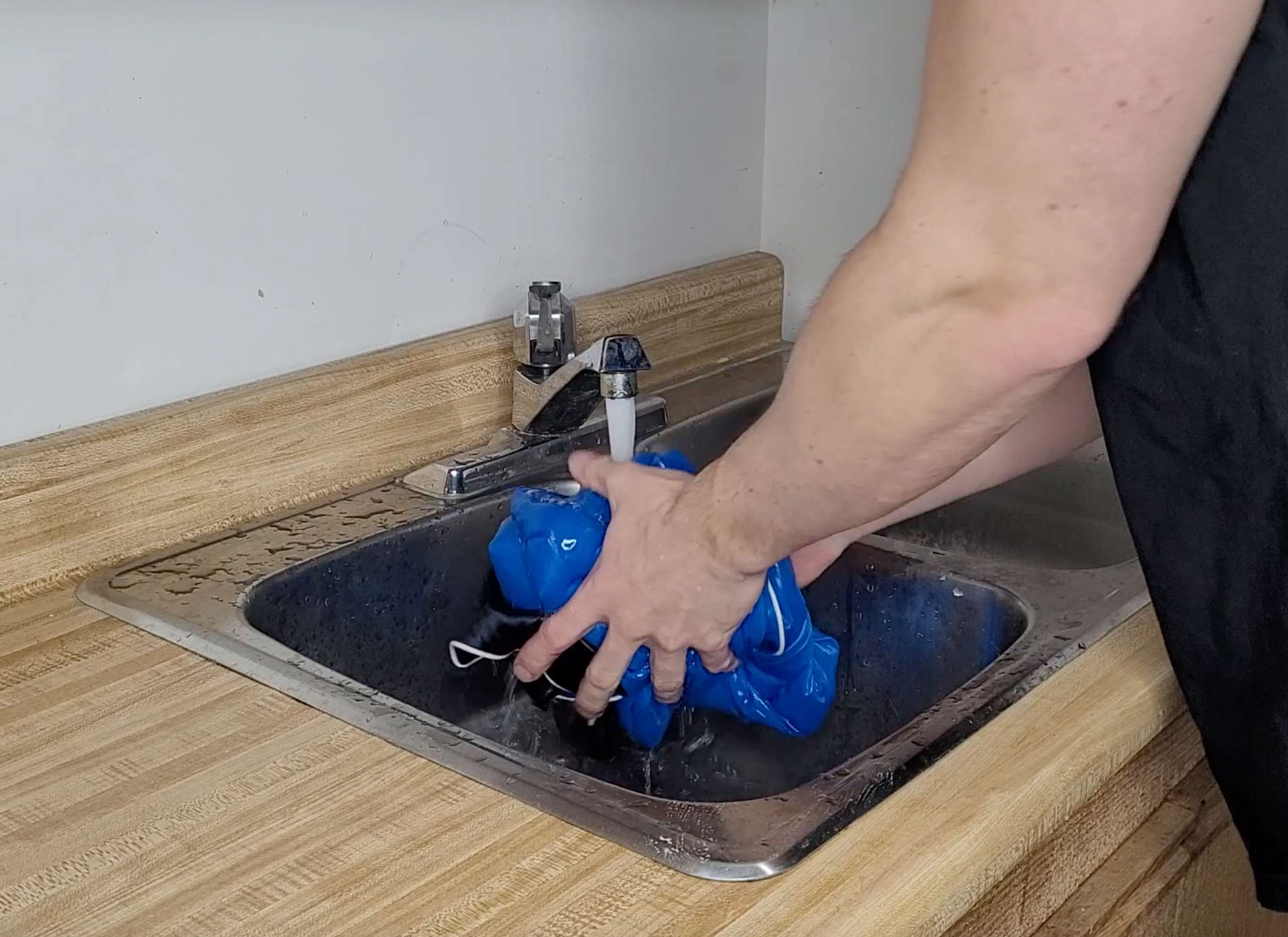 a picture of a man rinsing a blue silk shirt under a tap running cold water