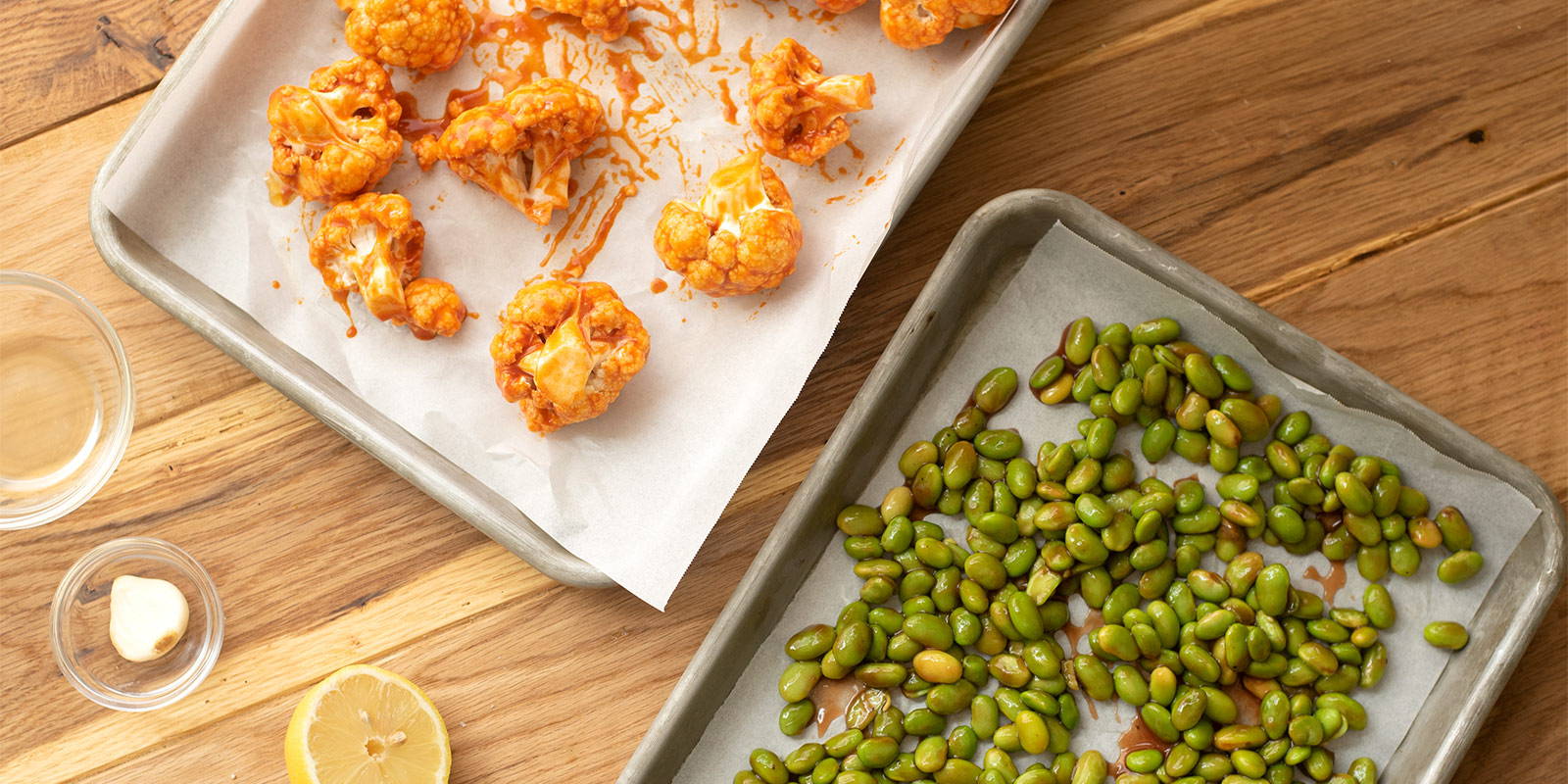 Two parchment paper lined trays, one featuring cauliflower and the other edamame.