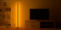 Eine Round Smart Lampe mit einem orangenen Farbübergang neben einem Bücherregal und einen Fernseher
