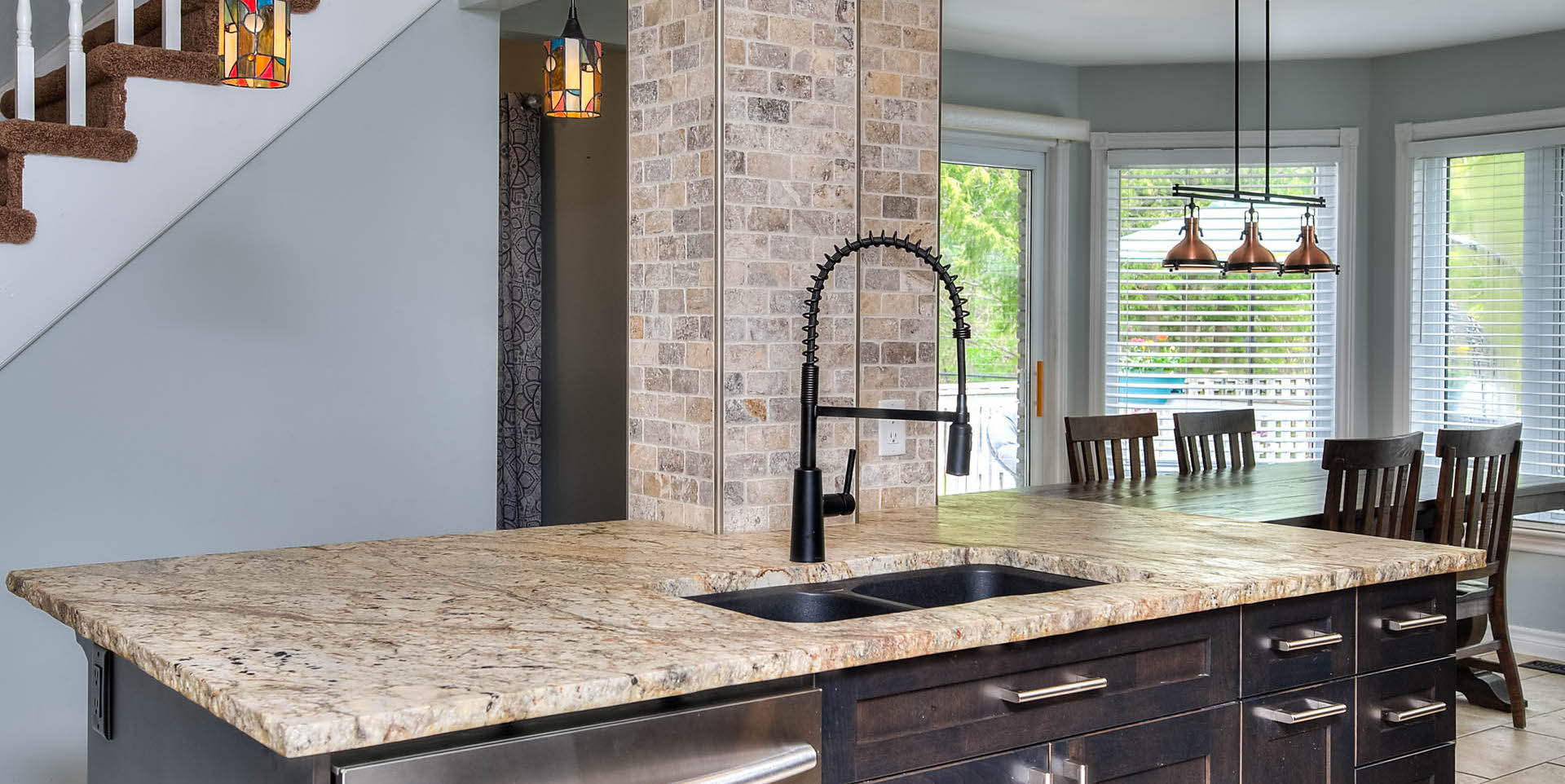 kitchen featuring tile flooring, natural light, dishwasher, pendant lighting, dark brown cabinets, and light stone countertops