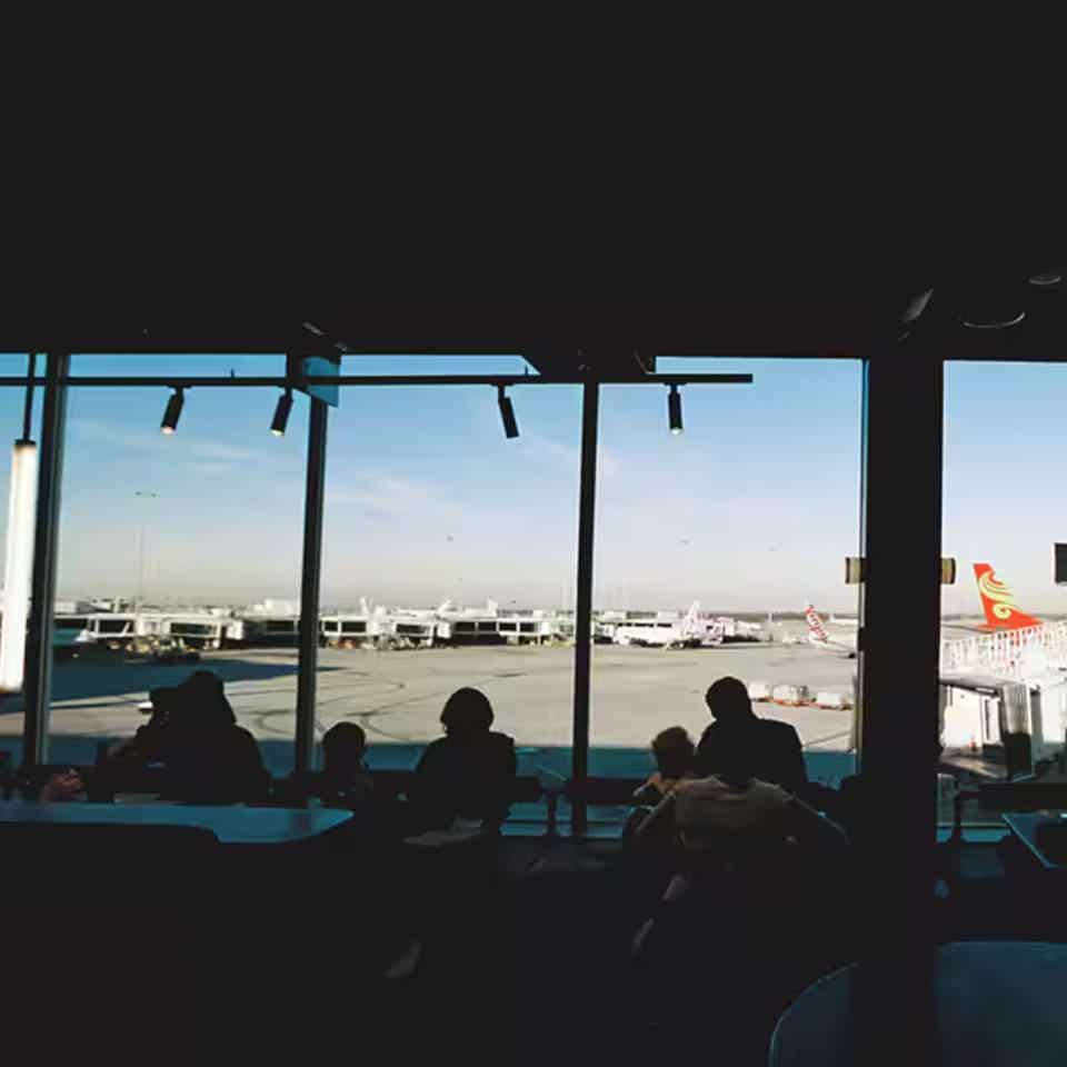 Dark interior of busy cafe with airport scenery of plane runways outside large glass window
