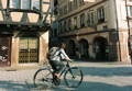 Une cycliste passe par les rues de Strasbourg sur son velo avec des maisons traditionnelles au fond