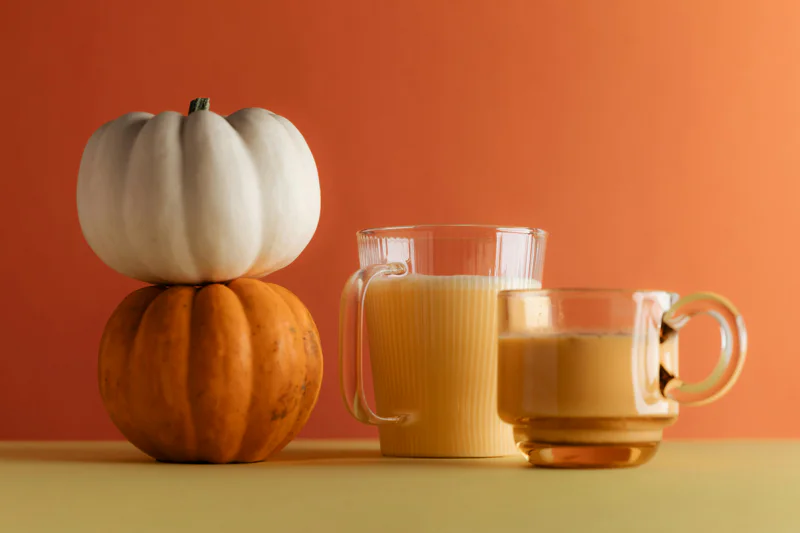 two latte drinks next to some pumpkins