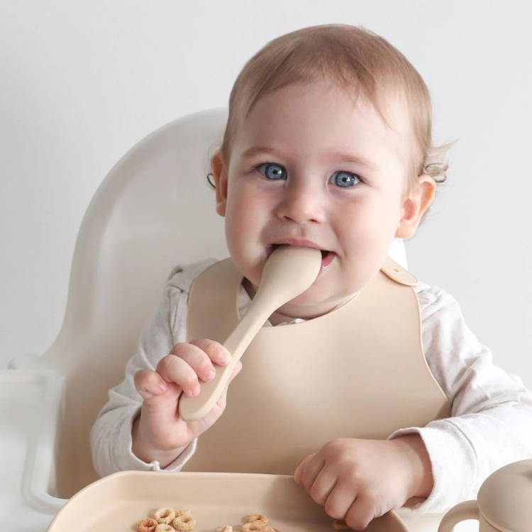Cute baby with blue eyes biting a silicone spoon from the Montessori First Bites Gift Set.