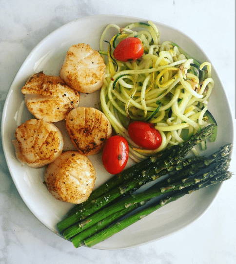 A plate with sautéed scallops, zucchini noodles, cherry tomatoes, and asparagus.