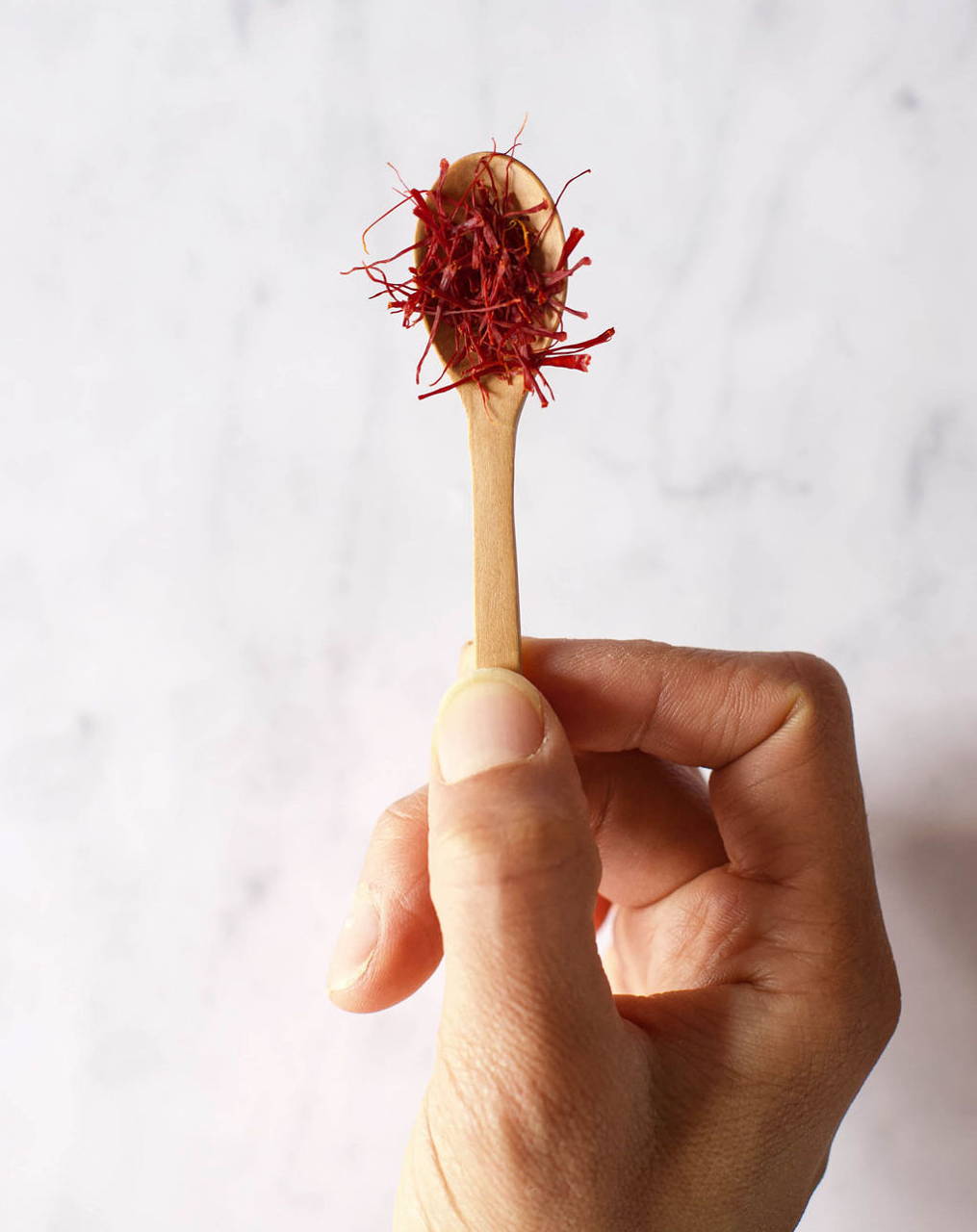 A pinch of saffron sits on a small wooden spoon above a white granite counter