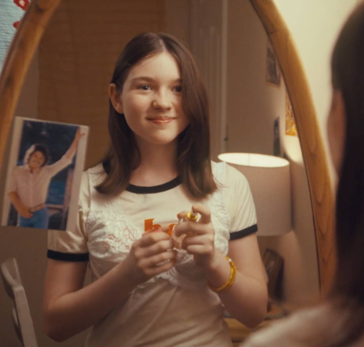 Young girl, smiling, in front of mirror applying some Love's Baby Soft coologne on her.