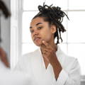 Model looking at herself in a mirror pointing to the Clear Skin Days blemish patch applied to the side of her face