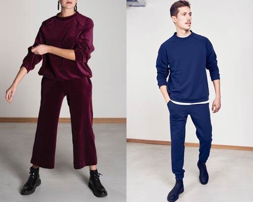 Woman wears organic cotton burgundy velvet sweatshirt and matching wide leg cropped trousers and man wears blue jersey sweatshirt with matching sweatpants from sustainable fashion brand Jann 'n June