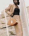 Black female model holding a NOIRANCA handbag Alice in Brown, walking through a white door