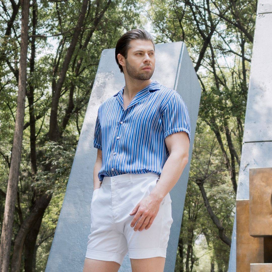 model walking through a plaza wearing white shorts and a short sleeve blue stripe silk shirt from 1000 kingdoms