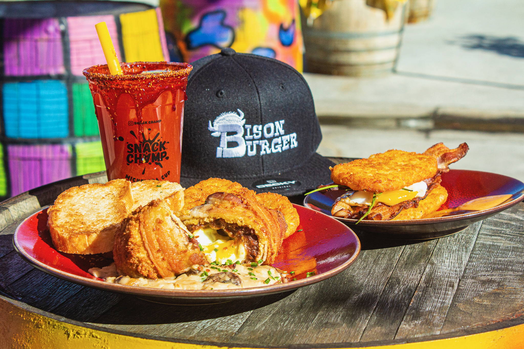 two plates of brunch food with a Snack Champ michelada and a black flat bill hat with Bison Burger logo embroidered in white