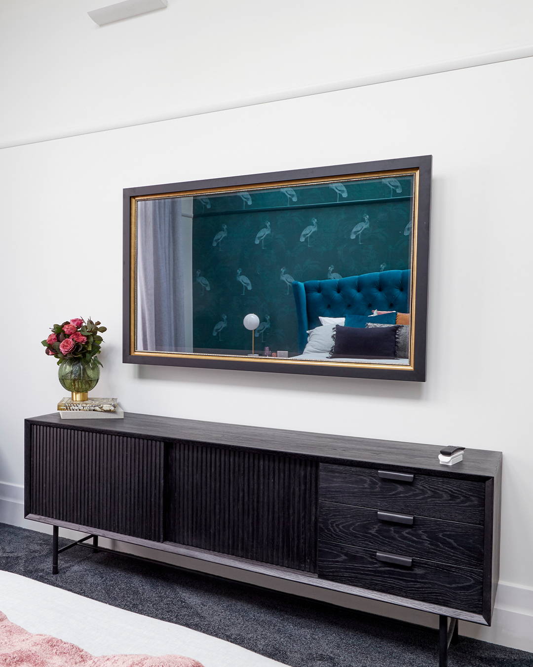 A TV-Mirror in a black and gold frame in a light-filled bedroom setting.