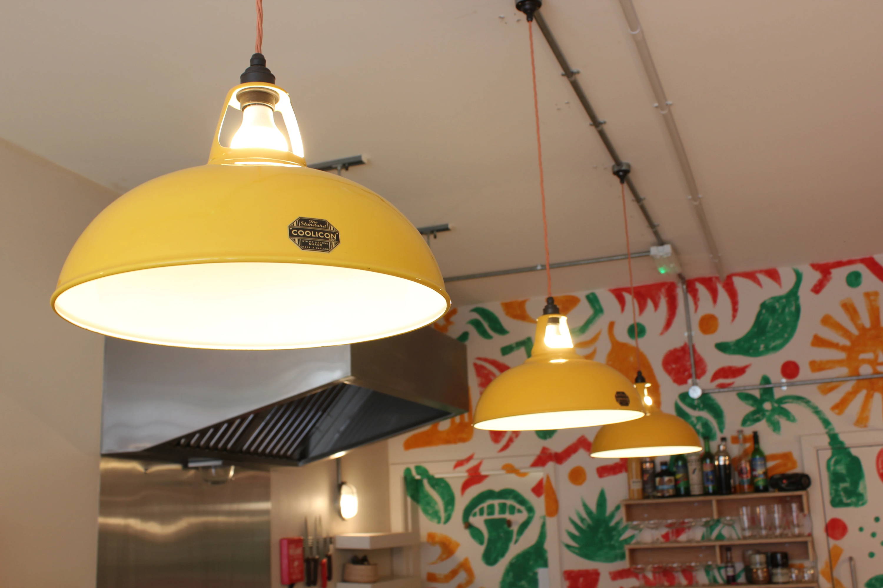 Three large yellow Coolicon lampshades with black lampholders and a red cable are hanging in a row.