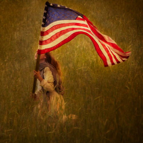 Little girl happily running through the field with an American flag.