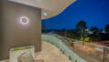 Balcony Havit circular LED wall light illuminating curved balcony with glass balustrade and coastal night view, Manly QLD