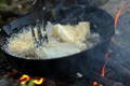 fish frying in a cast iron pan over a fire