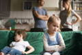 Children sitting on a sofa while parents are arguing in the back.