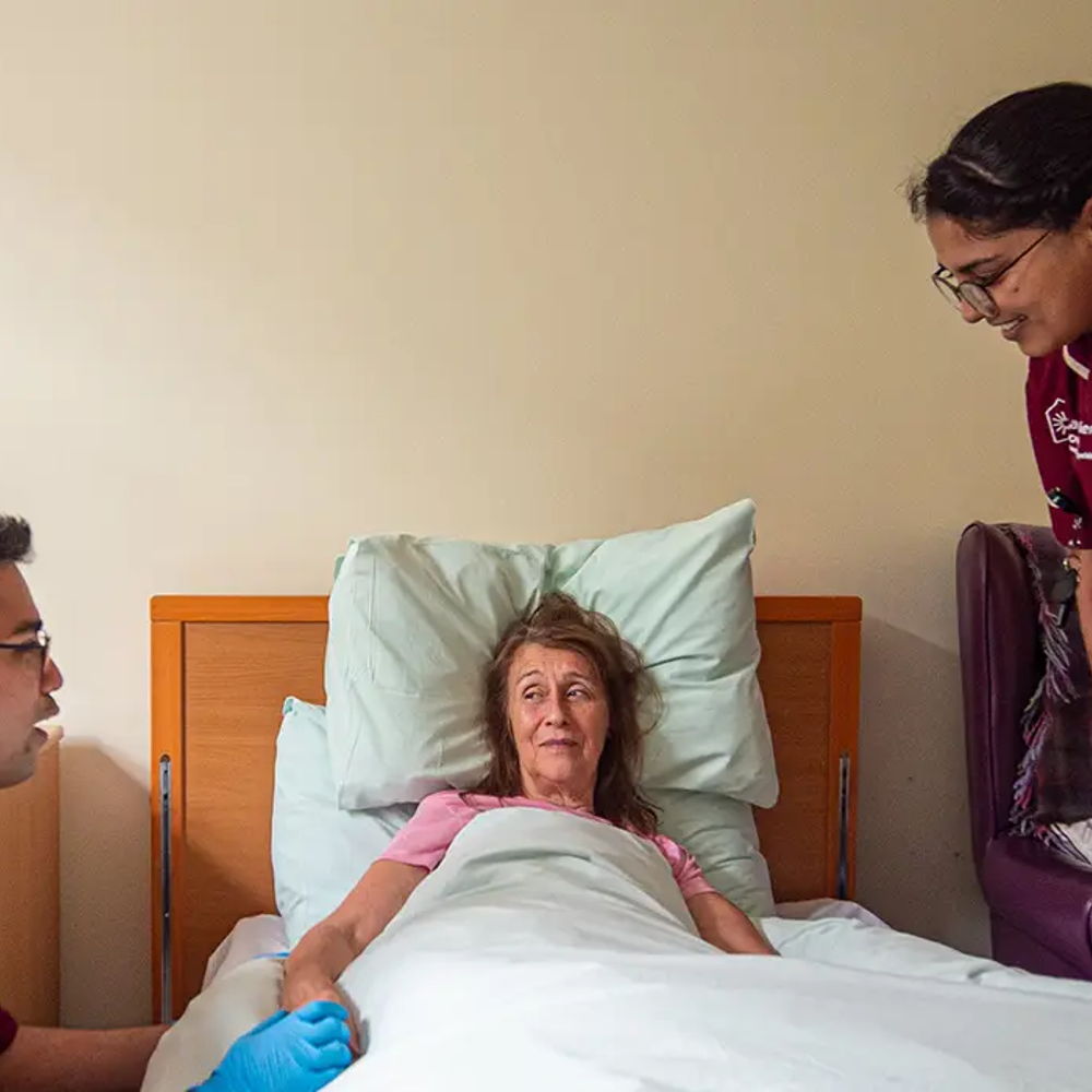 Two Larchfield House nurses assist a resident as she lays in bed.