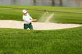 Golfer executing a bunker shot, blasting sand on the green.