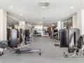 Ein geräumiges, modernes Fitnessstudio mit Kraftgeräten, Rudergerät und Hanteln vor verspiegelten Wänden.