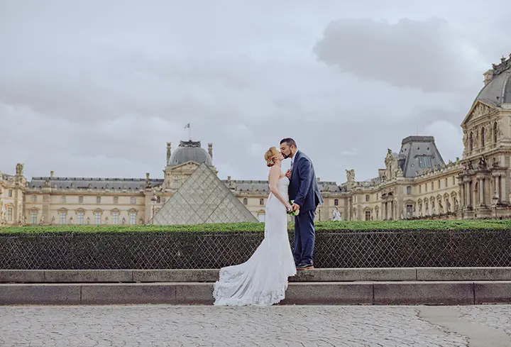 Photo de la mariée et du marié devant le musée du Louvre en train de s'embrasser.