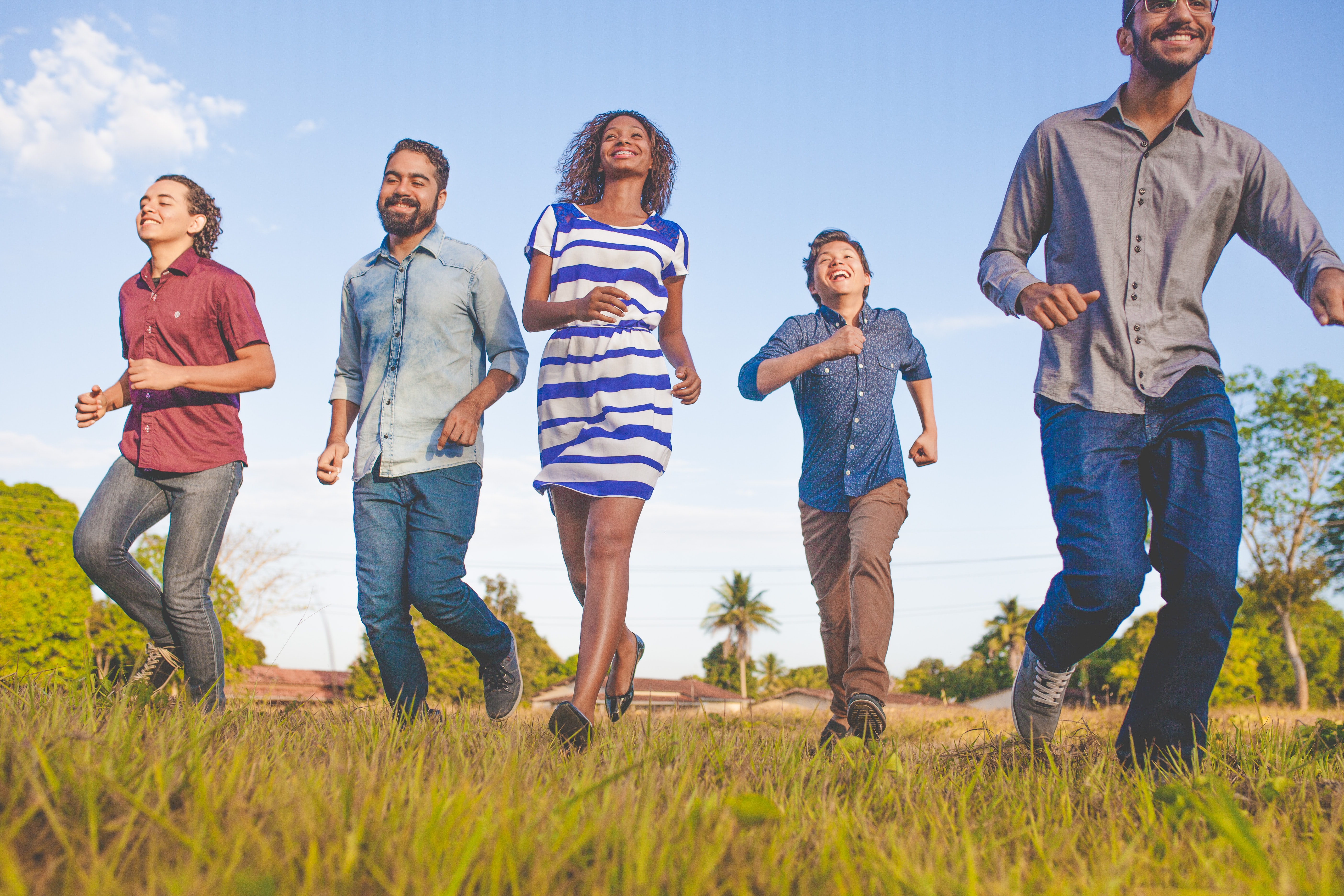 An ethnically diverse group of friends in casual clothes walking through a field toward the camera.