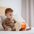 Cute baby sitting on the bed and looking at the wooden Montessori Spinning Drum.