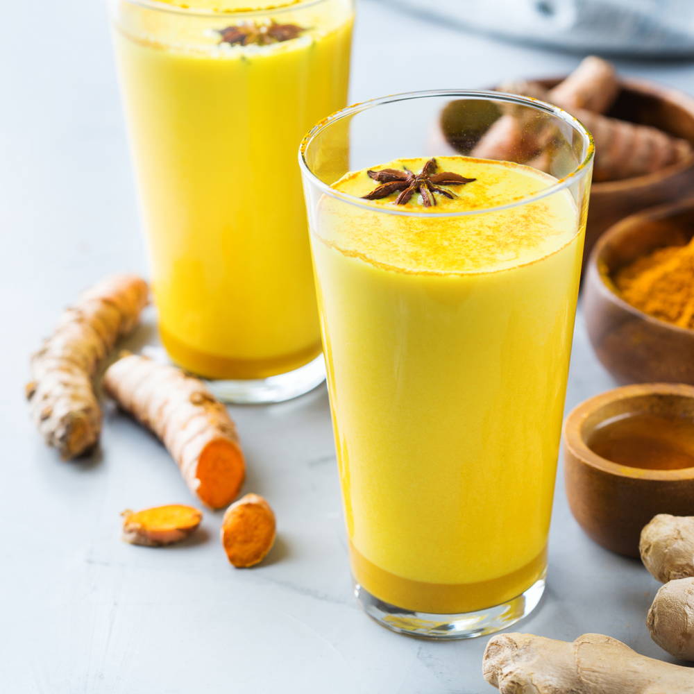 Glass of turmeric shake with turmeric root next to it