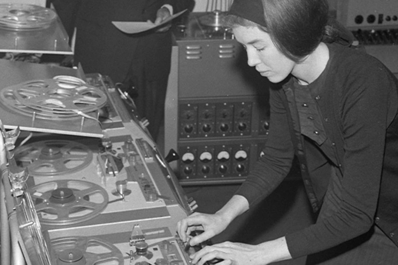 A black and white picture of Delia Derbyshire holding buttons of a mixing table