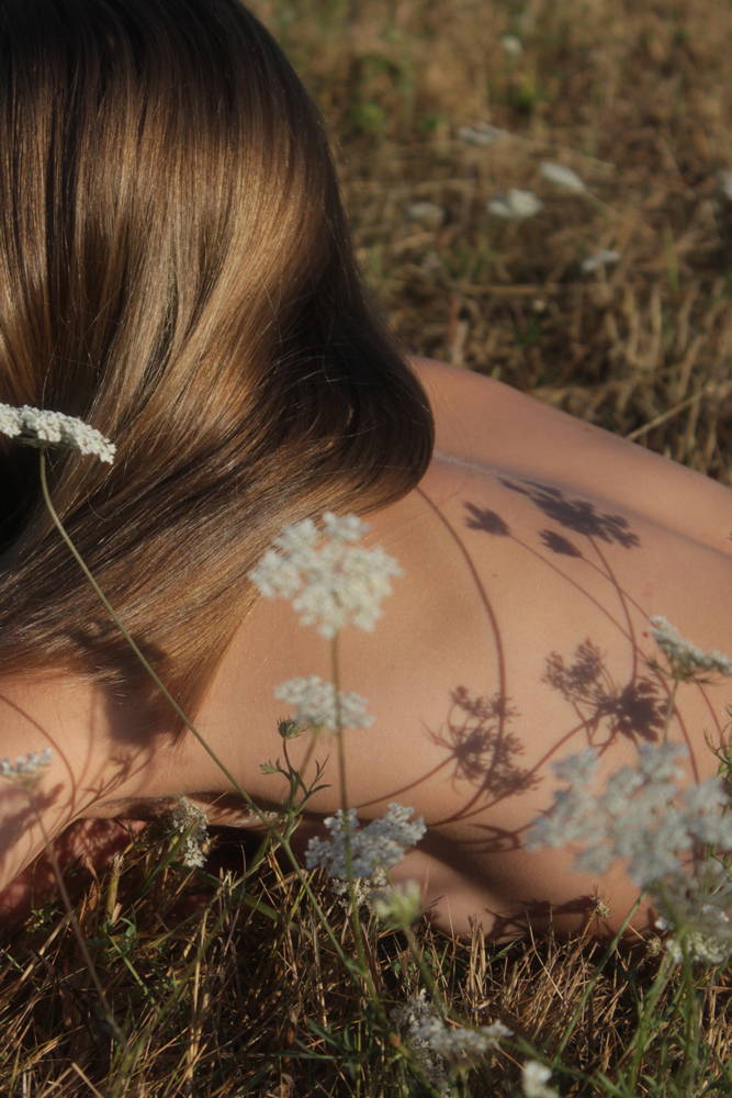 Woman lies in a meadow with flowers and the sun on her back