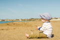 Baby sitting on a beach and looking towards the sea. 