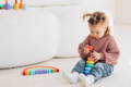 Little girl sitting ion the carpet and playing with colorful Montessori stacker toy.