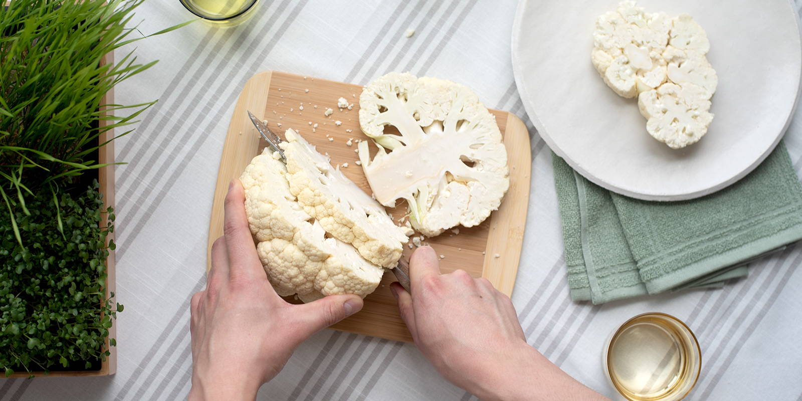 A head of raw cauliflower being sliced into thick grillable-slices