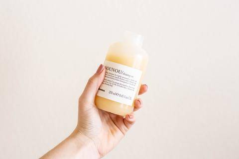 a hand holding Davines NOUNOU shampoo in front of a neutral background