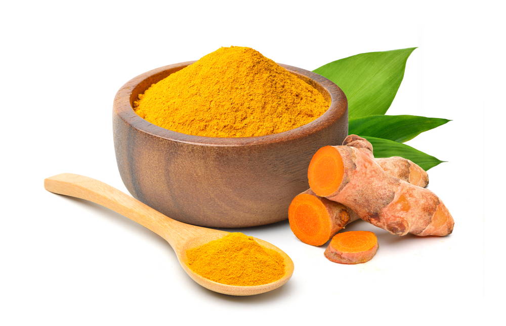 Turmeric powder in a wooden bowl beside a spoonful and turmeric root