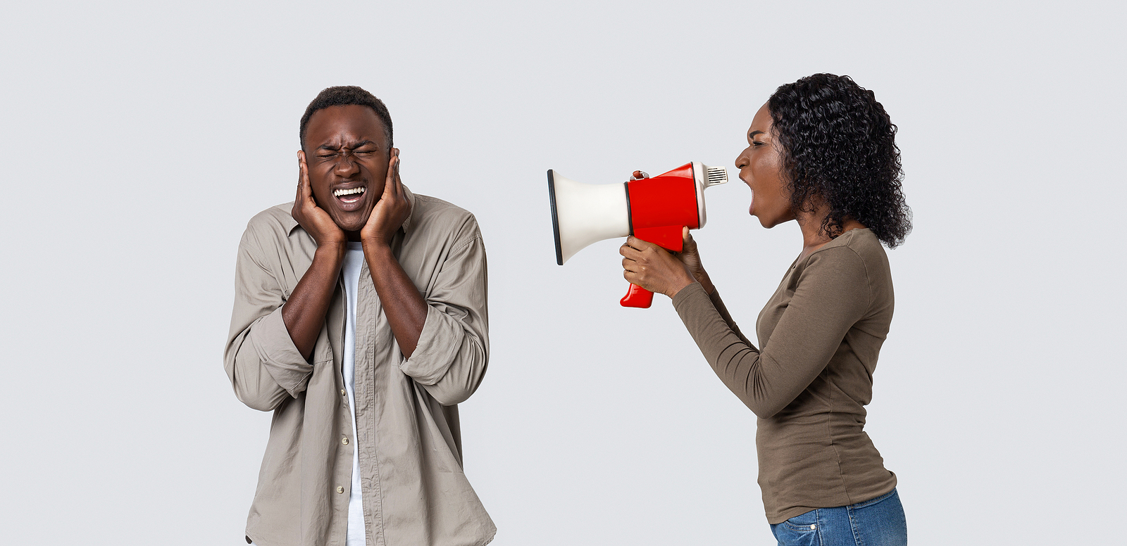 A woman yells at a man through a megaphone, he is wincing covering his ears.