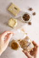 A set of hands carries a pouch of Cinnamon while topping off a half full jar