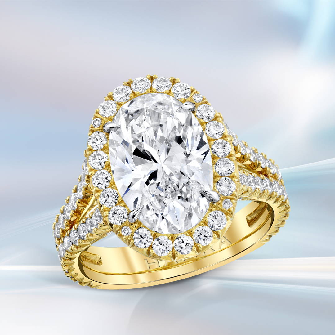 Oval shaped diamond engagement ring with diamond halo and split shank in yellow gold on a bluish background.