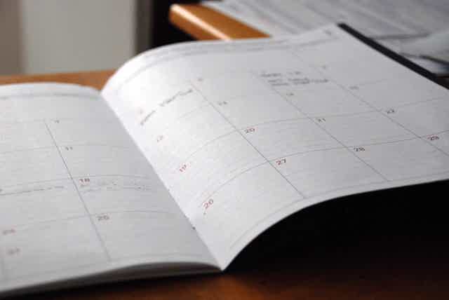 Open desk calendar with dates and grid lines, pages slightly curved, on wooden surface.