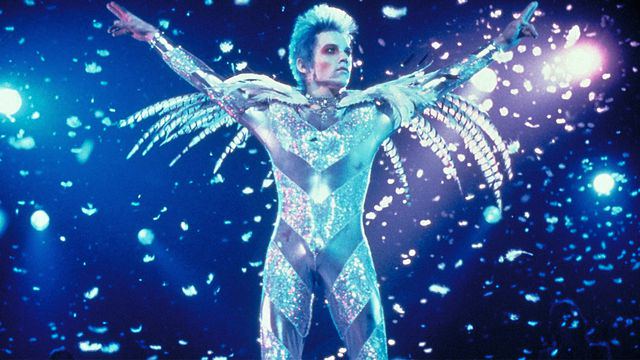 Brian as Tommy Stone wearing an elaborate silver and glitter costume with feathers performing onstage.